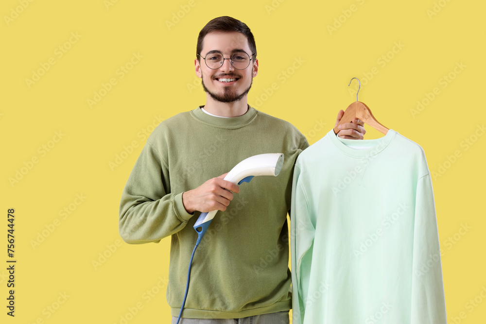 Happy young man steaming shirt on yellow background