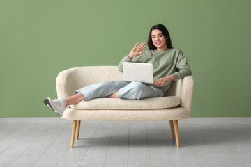 Canvas Print - Beautiful young happy woman with laptop lying on comfortable sofa and video chatting near green wall