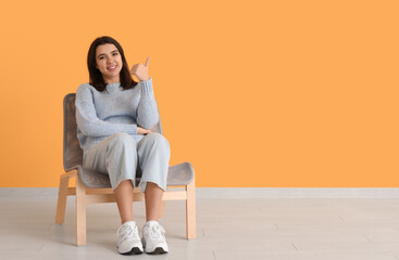 Canvas Print - Beautiful young happy woman sitting on comfortable chair near yellow wall