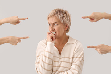 People pointing at worried mature woman on light background. Accusation concept