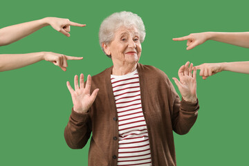 People pointing at senior woman on green background. Accusation concept