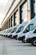 © Degimages - A fleet of delivery vans lines up outside a distribution center, ready to transport packages to customers.