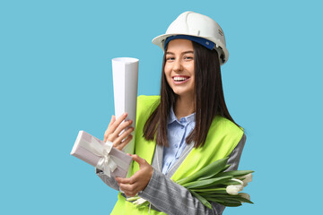 Canvas Print - Female construction worker with house plan, gift box and white tulips on blue background. Women's Day celebration