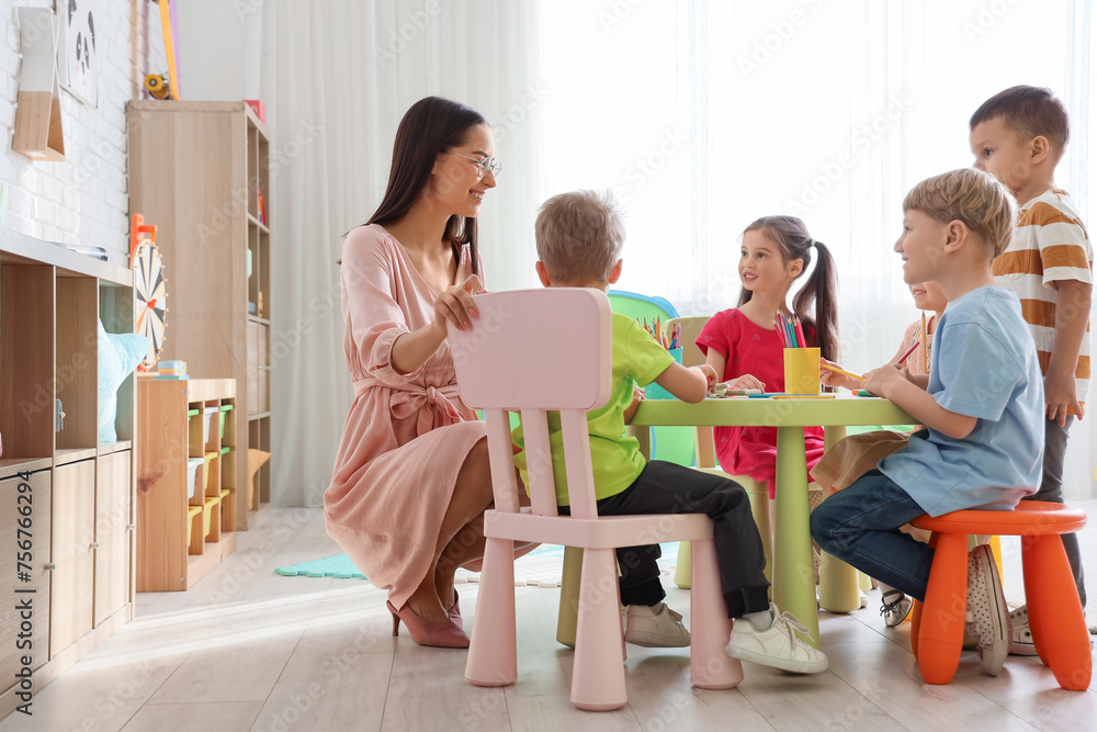 Little children with nursery teacher drawing at table in kindergarten