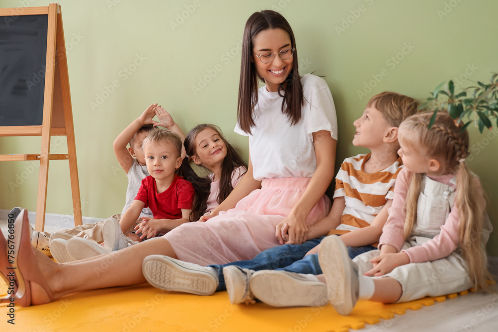 Little children with nursery teacher sitting in kindergarten