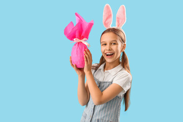 Wall Mural - Cute little girl with Easter bunny ears and gift on blue background