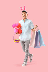 Wall Mural - Young Asian man in bunny ears with eggs and shopping bags on pink background. Easter Sale