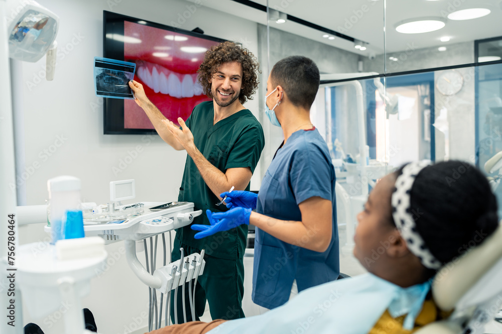 Smiling positive male dentist in a dental office talking with a female colleague while showing a x-ray image of a patient's teeth in a modern dental clinic.