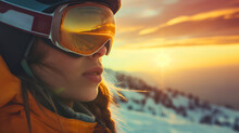 Closeup of the young woman wearing a jacket, skiing or snowboarding googles and equipment, standing on the snowy trail during the cold winter season day outdoors, smiling at the camera. Sunset