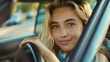 Closeup of the beautiful young woman with blonde hair driving a car in the city traffic, smiling at the camera. Downtown automobile transport, sitting in a vehicle interior and holding steering wheel