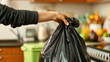 Woman holding the black plastic bag full of trash in her hand, standing in a modern kitchen interior. Home environment garbage or waste disposal, household hygiene utilization