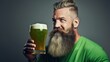 Bearded man in a green shirt holding a mug of green beer against a dark grey background. St Patricks Day