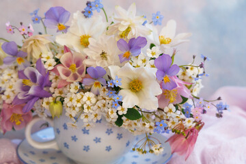 Poster - Bouquet of spring and summer flowers in a cup on the table, aquilegia, spirea, anemone, forget me not flowers, pansies, violet, beautiful postcard, closeup, blur.