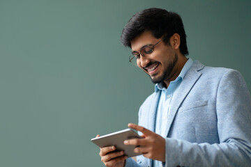 Happy hindu businessman websurfing on digital tablet against green wall