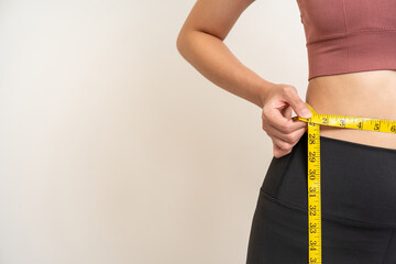 Close up woman measuring her waistline with measure tape. Weight loss diet session. Woman in sportswear slim fit and firm body shape. Care about eating and workout exercise.