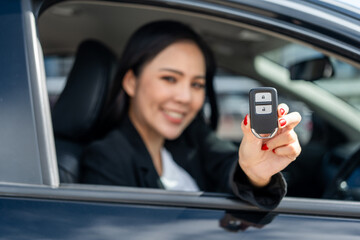 Wall Mural - Young beautiful asian business women in suit getting new car showing car key. she very happy and excited in hand holding car key. Smiling female driving vehicle on the road city on a bright day