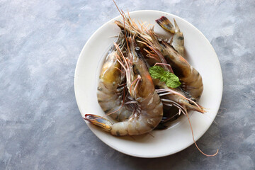 Wall Mural - Fresh shrimp or black tiger prawns. Uncooked on a white ceramic plate with coriander and mint leaves. on a moody background with copy space. Kolambi in Marathi.