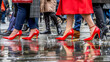 A close-up of pedestrians, including women in high heel stilettos, walking along a rain-soaked street.