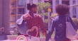 Multiple pink heart icons floating against african american couple holding hands while walking