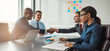 © Flamingo Images - Two diverse business teams sit at a conference table and shake hands on reaching an agreement. They all smile at having made a business deal
