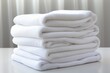 A neat pile of pristine white beach towels rests on a plain white surface