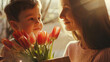 Cute lad with bunch of beautiful tulips looking at his mother with giftbox, mothers day concept