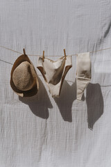 Female swimwear and straw hat hanging over white cotton cloth with strong shadows. Sunbathing on a summer sunny day concept