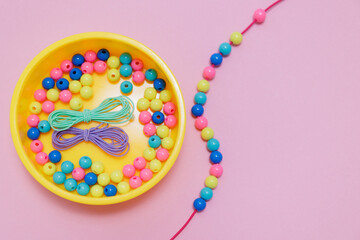 Box with multicolored beads and handmade kids jewellery on pink background