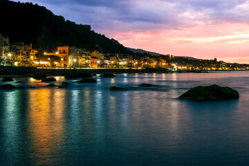 Wall Mural - evening or night landscape of evening town coastline in golden lights and sea gulf with calm water and nice reflections with beautisul sunset sky on background