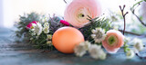 Fototapeta Tulipany - Easter egg in front of a herb nest with spring flowers on weathered rustic wooden table. Close-up with short depth of field. Horizontal easter background.