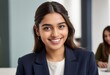 © kotlyarn - An approachable young woman smiles at the camera in a business setting. She's wearing a navy blue blazer.