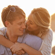 © peopleimages.com - Couple, sunset and hug for love by water, ocean waves and peace for romance in relationship. Happy people, looking and security in marriage, embrace and travel on vacation or holiday for outdoor date