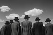 Black and white photograph: men stand in suits and hats with their backs looking at the sky with clouds