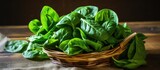 Fototapeta Las - A basket filled with spinach leaves, a leaf vegetable, sits on a wooden table. Spinach is a popular ingredient in many dishes across cuisines