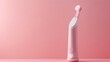 A sleek pink electric toothbrush laying on a soft pink background