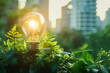 A glowing electric light bulb stands on the ground among green plants against a backdrop of blurred city buildings. Concept of green energy and ecology.