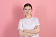 Portrait of a sad brunette girl, Caucasian young woman in a casual white t-shirt with arms crossed, sulking and frowning with disappointed isolated on a pink studio background.