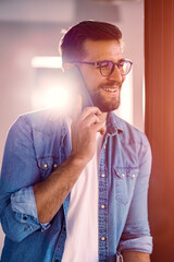 Wall Mural - Handsome young man with glasses standing in the office and using the phone.