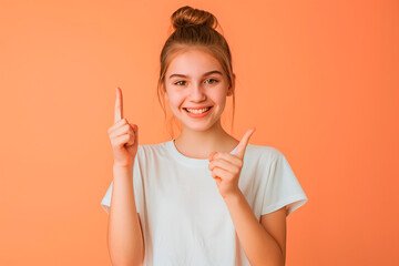 Wall Mural - Portrait of a young girl points her finger to the side on a peach background. Copy space