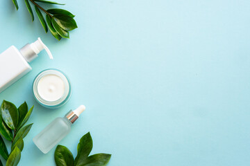 Wall Mural - natural cosmetic products flat lay on blue. cream, soap and serum with green leaves.