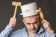 A perplexed man with a saucepan on his head is trying to find the right thoughts with the help of a hammer and rolling pin.