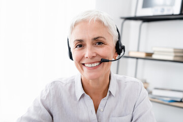 Cropped shot of Caucasian mature businesswoman in headset looking at camera in office. E-learning, telework, saleswoman manager, hotline worker, IT support manager