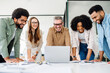 © Vadim Pastuh - A diverse team of professionals is seen deeply engrossed in a laptop presentation, reflecting a moment of shared focus and collaborative analysis in a dynamic office setting