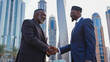 Two african business men engaged in a firm handshake against the backdrop of a bustling urban environment. The setting appears to be a financial or business district characterized by modern 