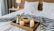 Hygge concept Coffee and candle filled wooden tray on a bed accompanied by white bedding striped blanket and pillow serving breakfast