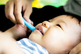 Fototapeta Sawanna - Boy doesn't like brushing his teeth and is sad, baby with her mother and brushing teeth