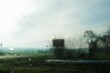 Abstraktes Motiv mit Wassertropfenmuster auf beschlagener Glasscheibe vor grüner Landschaft mit Ackerfeldern, Bäumen, Haus und Himmel bei Sonne, Frost und Regen am Morgen im Winter