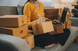 © ARMMY PICCA - Startup small business entrepreneur or freelance Asian woman using a laptop with box, Young success Asian woman with her hand lift up, online marketing packaging box and delivery, SME concept.