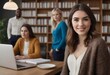 © natakot - Portrait of a smiling businesswoman at a desk with colleagues. Professional setting with bookshelves and laptop.