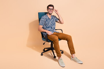 Sticker - Full length photo of handsome businessman touching specs sitting comfortable boss chair enjoying office isolated on beige color background